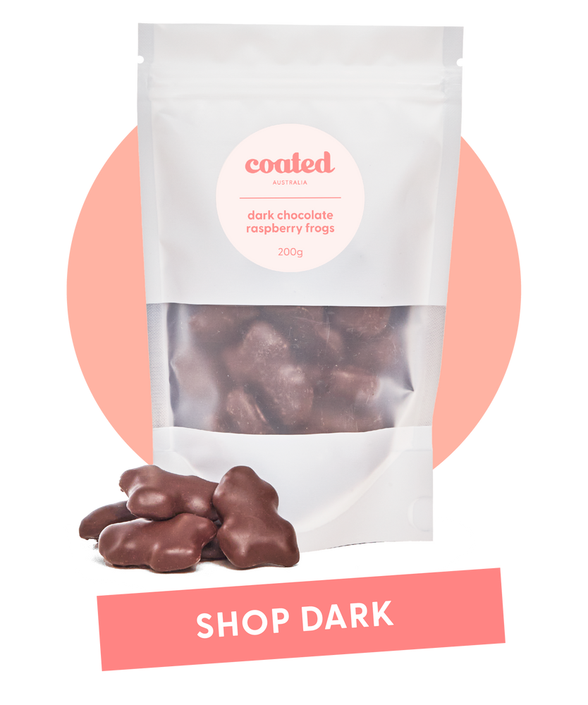 Coated Australia - Shop by Dark Chocolate. Dark Chocolate Coated products. Australian made. Made in Melbourne. Standing white bag, filled with dark chocolate raspberry frogs with a 'shop dark' title.