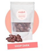 Coated Australia - Shop by Dark Chocolate. Dark Chocolate Coated products. Australian made. Made in Melbourne. Standing white bag, filled with dark chocolate raspberry frogs with a 'shop dark' title.