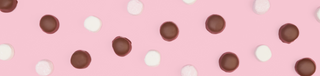 Chocolate coated marshmallows in milk chocolate scattered on a pink background.
