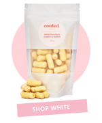 Coated Australia - Shop by White Chocolate. White Chocolate Coated products. Australian made. Made in Melbourne. Standing white bag, filled with white chocolate raspberry bullets with a 'shop white' title.
